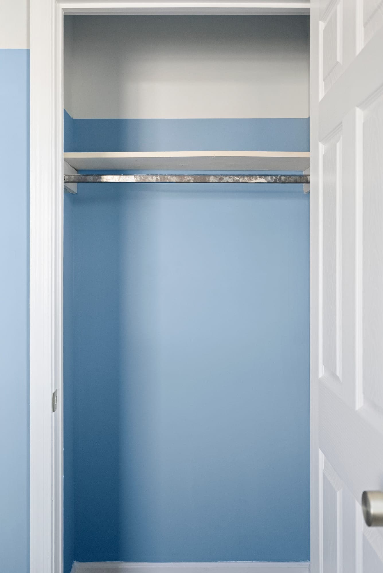 Reach-in closet freshly painted blue with a new shelf and hanging rod