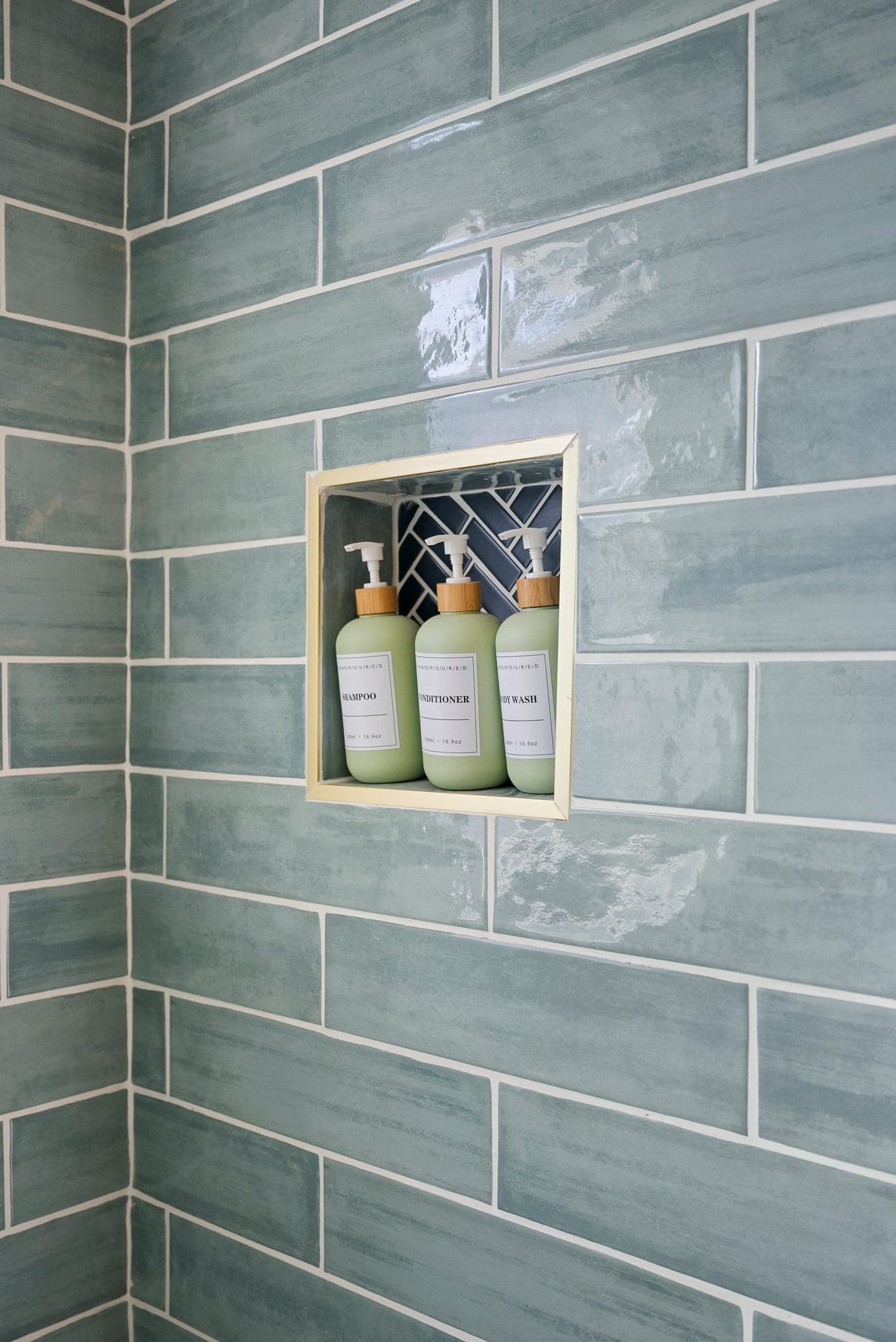 Blue-green glazed subway tile shower with a recessed niche trimmed in brushed gold